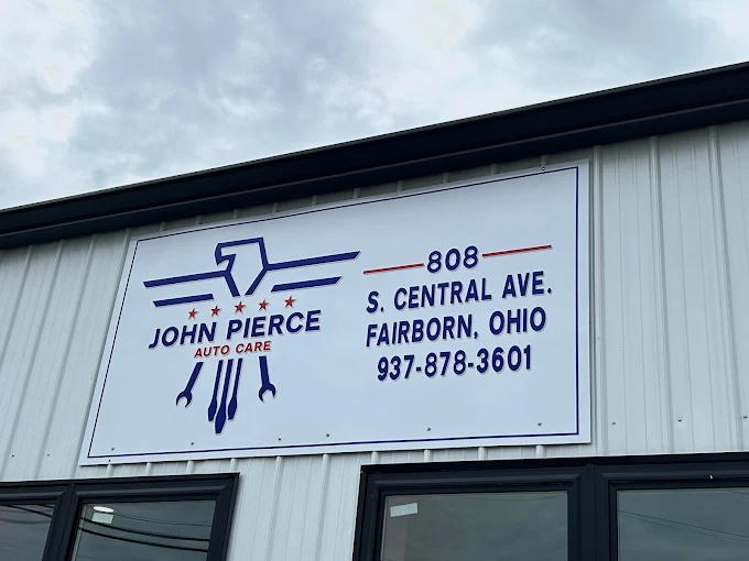 A white business sign with the company logo, name, and address mounted on a light grey building. The logo features a stylized hawk/eagle in blue above the text 